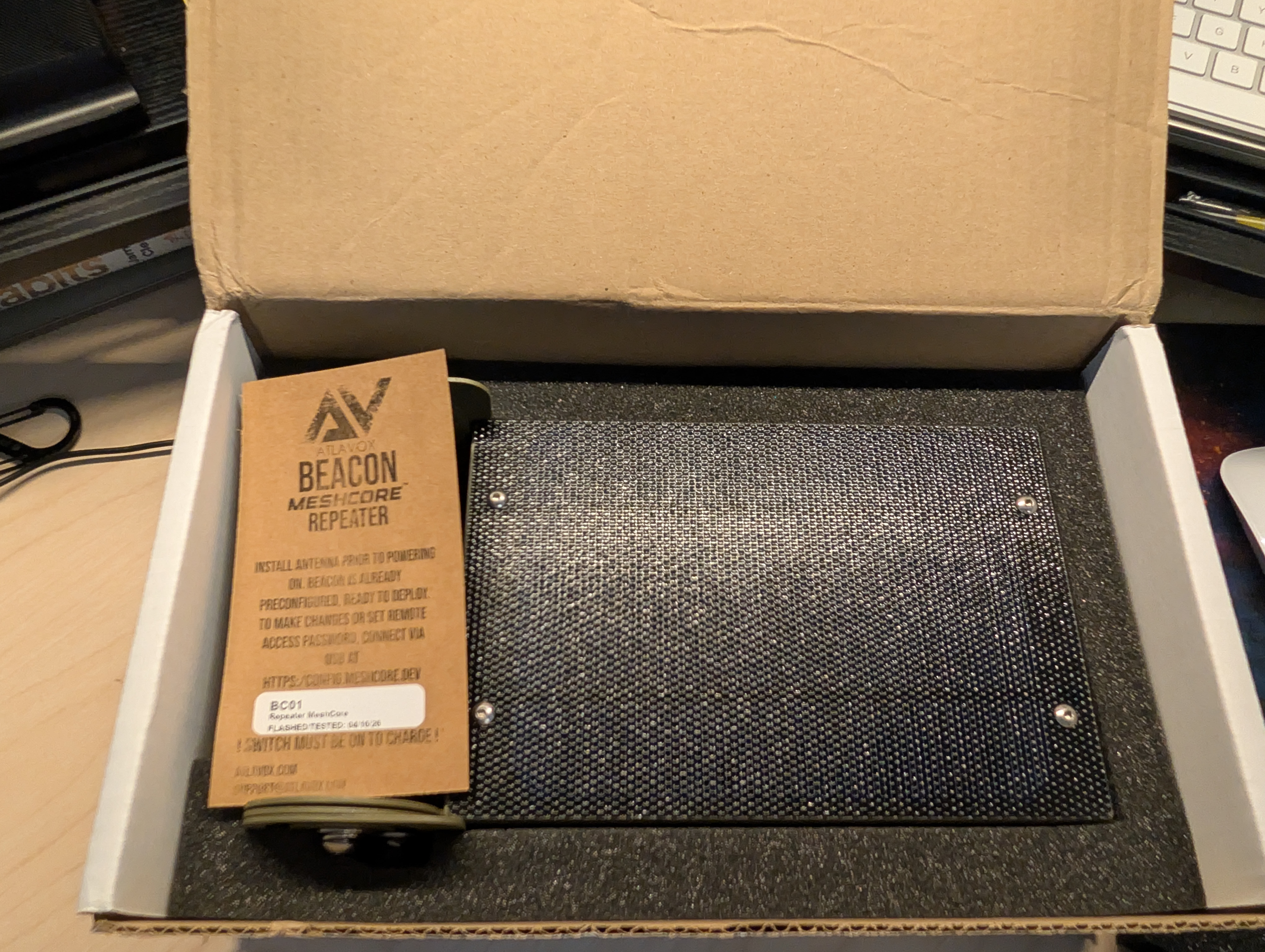 Atlavox Beacon shipping box opened, MeshCore Repeater instruction tag visible on the unit