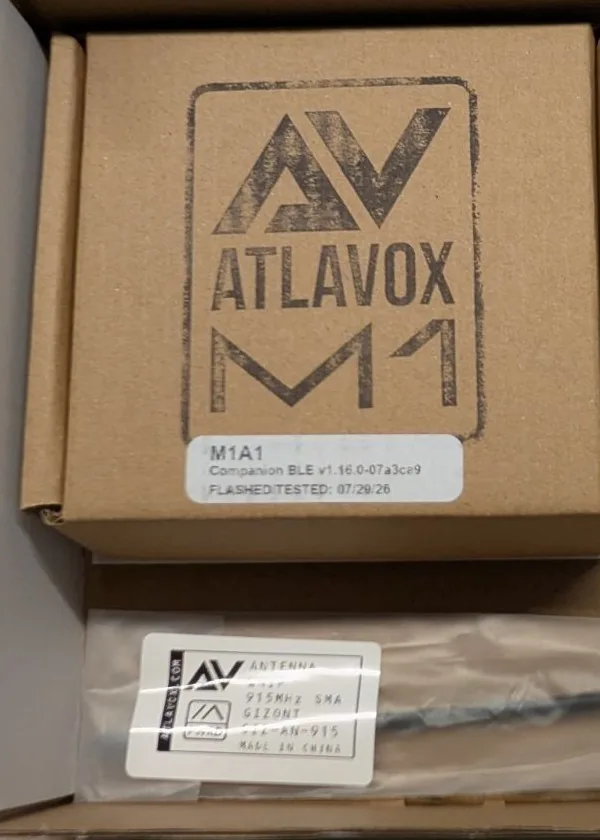 The Atlavox M1 inner box label reading M1A1, Companion BLE v1.16.0, flashed and tested 07/29/26, above a bagged Gizont 915 MHz whip antenna