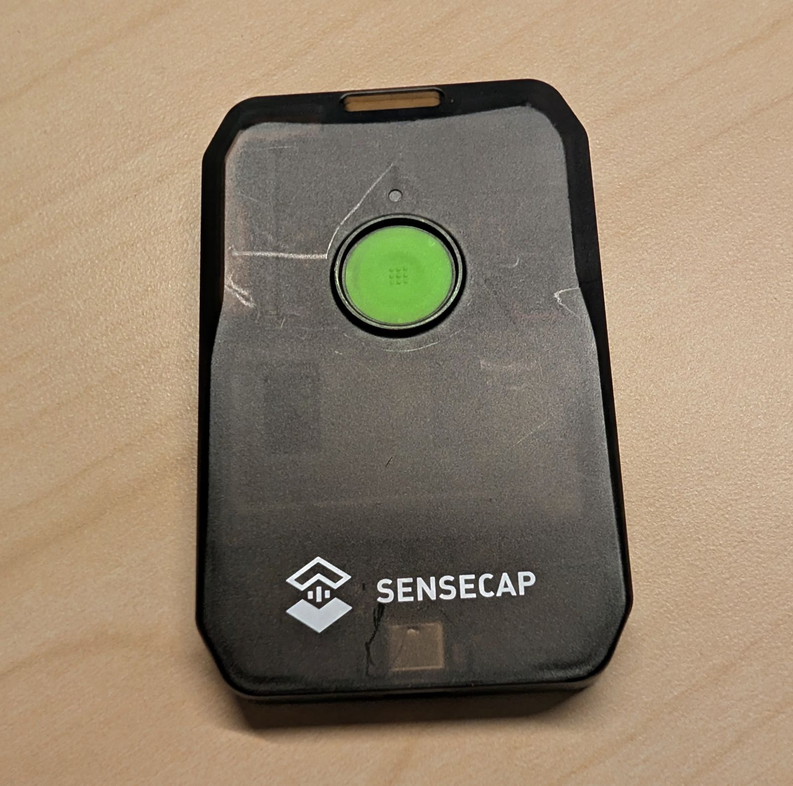 Close-up of the SenseCAP MeshTracker X1's front showing visible scuff marks and light scratching around the button after a month of daily carry