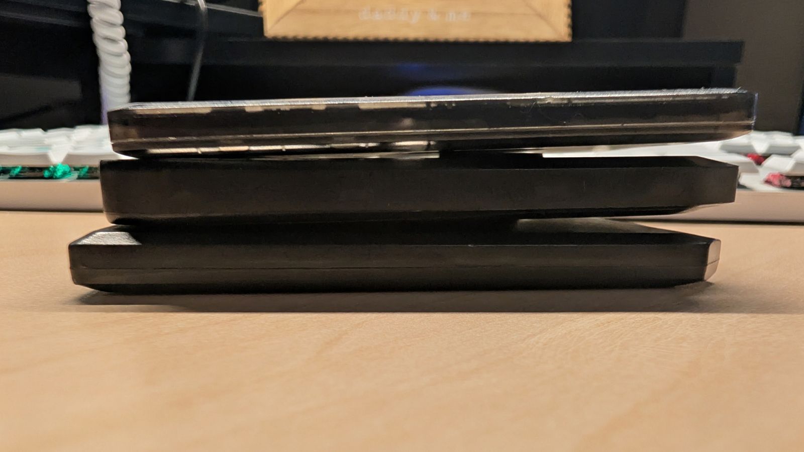 The three trackers stacked edge-on to compare thickness, top to bottom: SenseCAP T1000-E, MeshTracker X1, RAK WisMesh Tag, with the T1000-E visibly the thinnest of the three